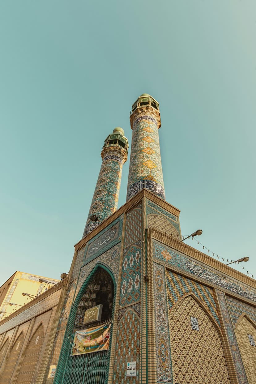 Two tall mosque minarets featuring blue tilework and calligraphy stand against a clear, vibrant blue sky.