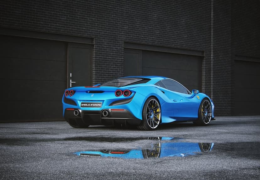 Blue Ferrari supercar parked on wet asphalt reflecting in a puddle against a dark brick industrial wall.