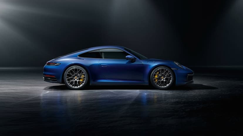 Profile of a metallic blue Porsche 911 with gold calipers in a dark studio with light reflecting off the floor.
