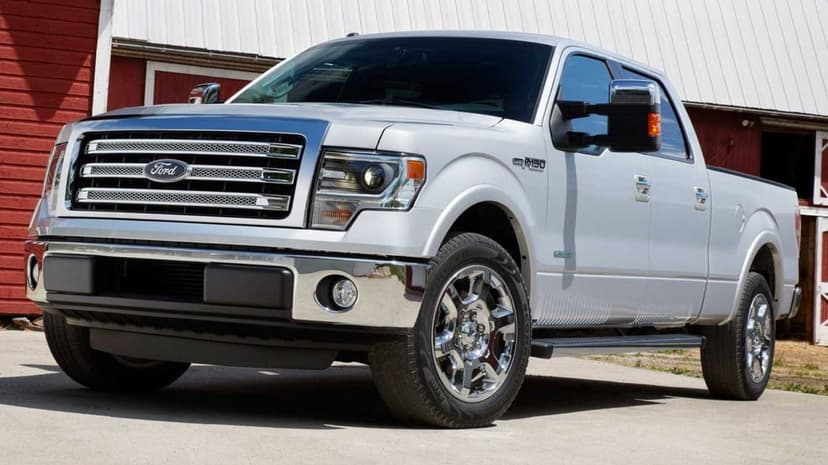 Silver Ford F-150 truck with chrome grille and headlights parked on concrete in front of a rustic red barn.