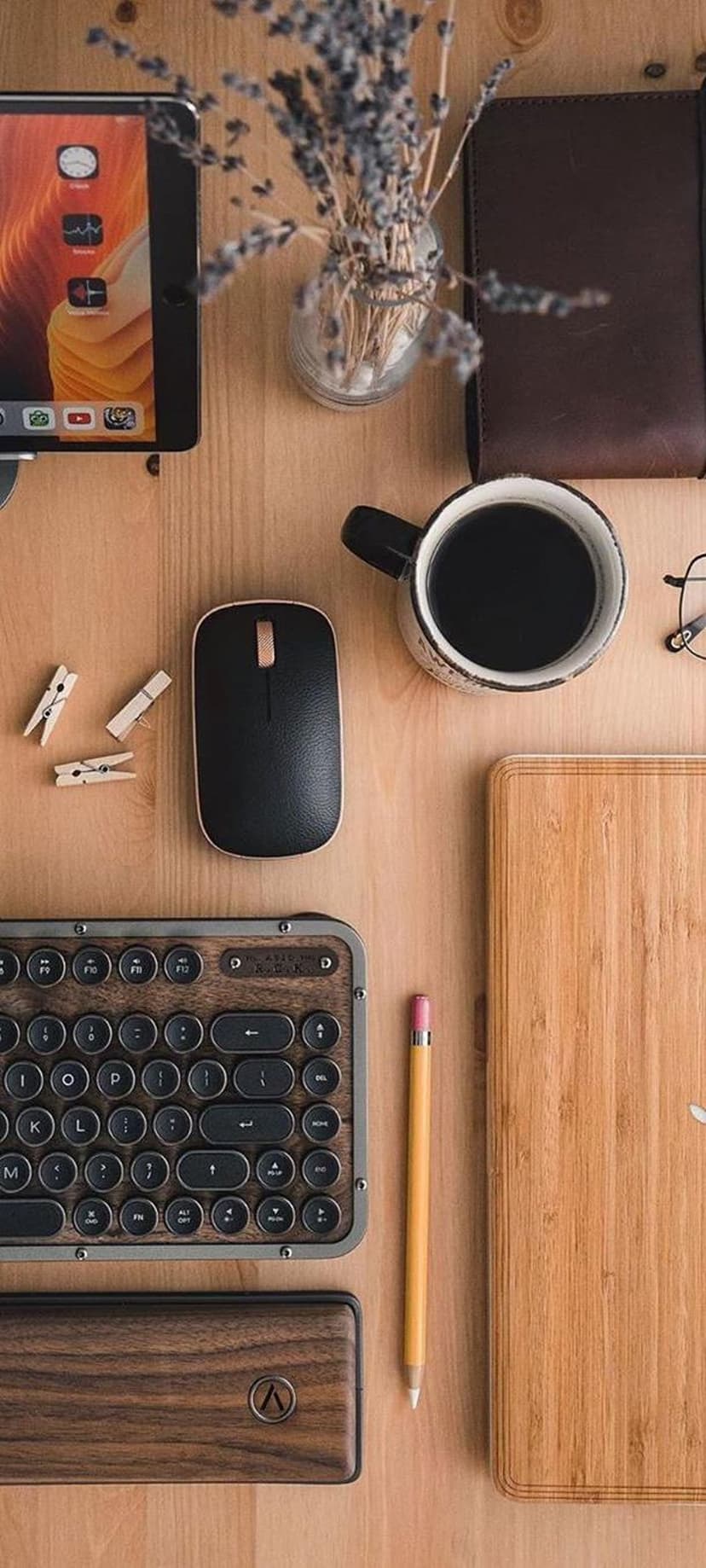 Vintage keyboard, black mouse, and coffee mug sit on a wooden desk next to a tablet and dried lavender stems.