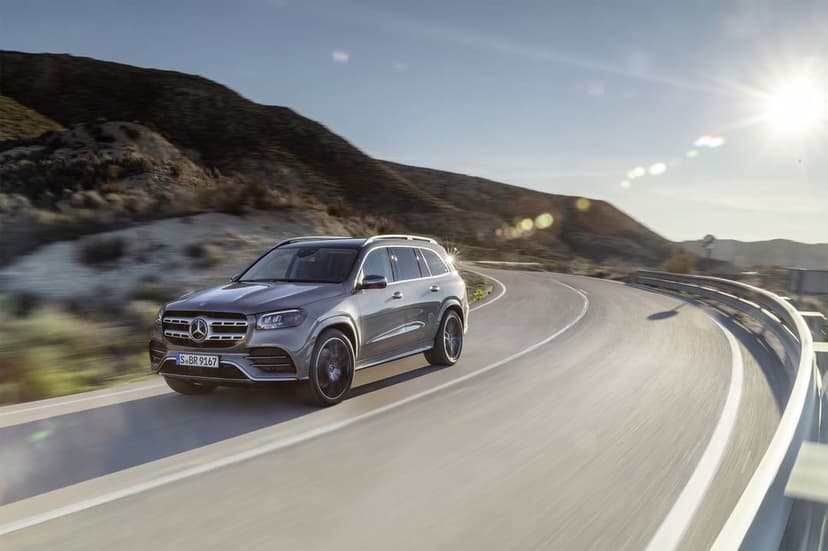 Grey Mercedes-Benz SUV driving on a winding mountain road with bright sun flare and motion blur.