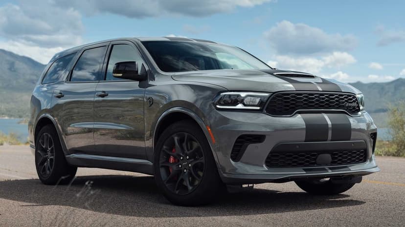 Gray Dodge Durango SRT Hellcat with black racing stripes parked on a mountain road with a lake background.