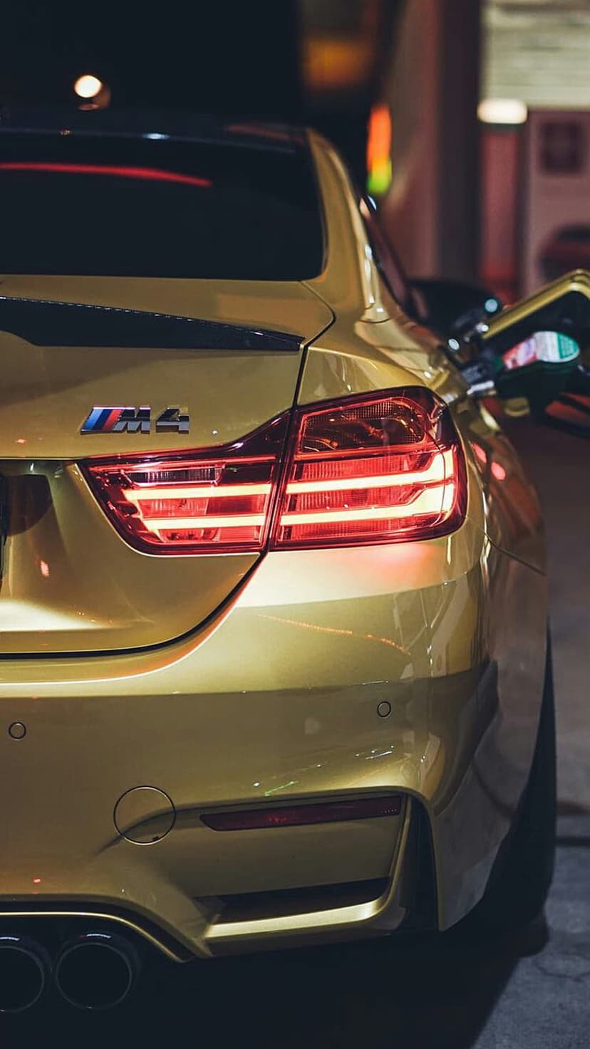 BMW M4 rear tail lights and emblem on a golden car body reflecting city lights in a nighttime urban setting.