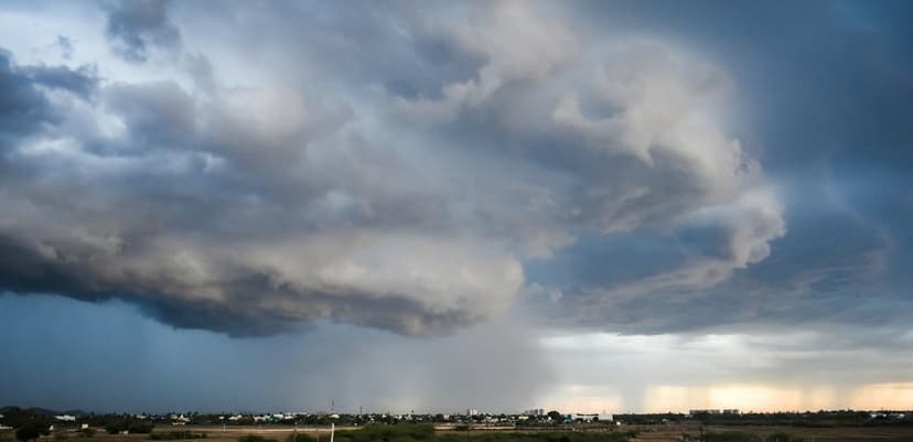 Dark nimbostratus clouds with a visible rain shaft hanging over a dry desert landscape during late sunset.