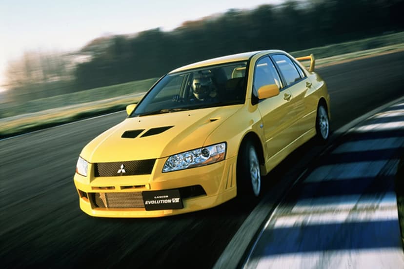 Yellow Mitsubishi Lancer Evolution VII racing on a track with motion blur and a driver wearing a helmet.