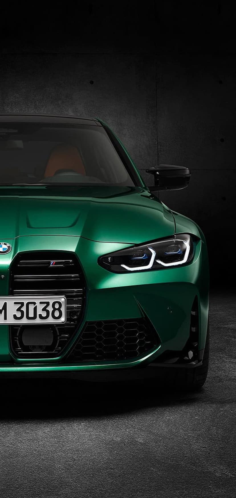 BMW M3 in Java Green featuring illuminated LED headlights and a black kidney grille against a dark backdrop.