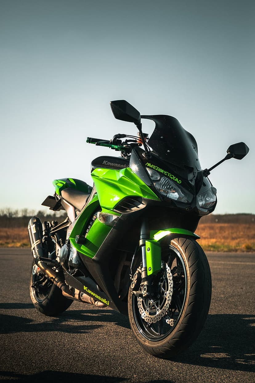 Green Kawasaki motorcycle with black windscreen parked on asphalt against a dry field and golden sunset sky.