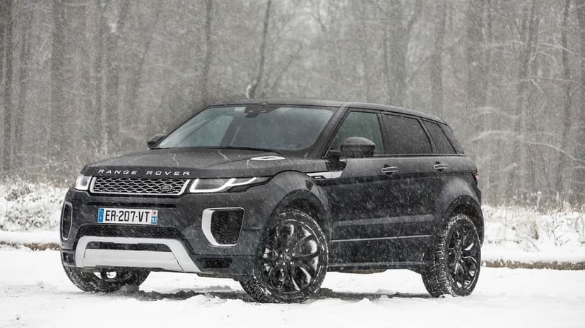 Black Range Rover SUV parked in a forest during a heavy snowfall with trees and white snow background.
