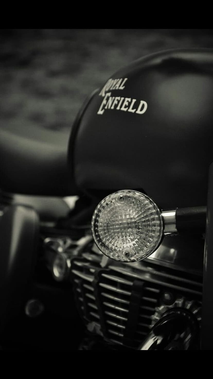 Royal Enfield logo on a fuel tank beside a round headlight and engine cooling fins in high-contrast monochrome.