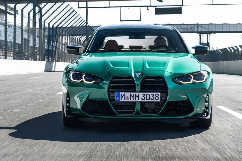 Green BMW M3 Competition driving on a sunny racetrack with motion blur and sharp blue laser headlights.