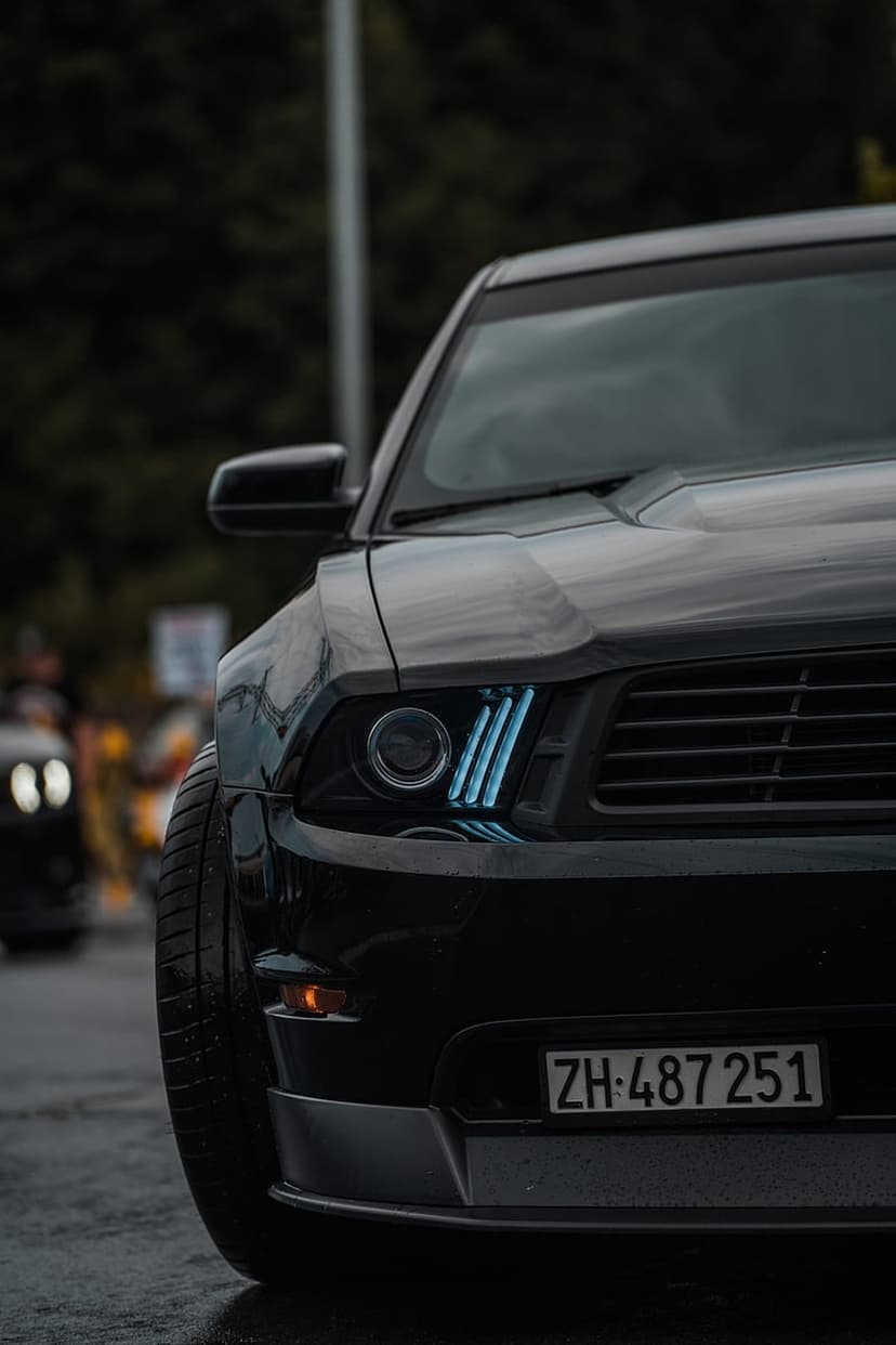 Ford Mustang front bumper and blue LED headlights reflecting on wet asphalt during a moody night scene.