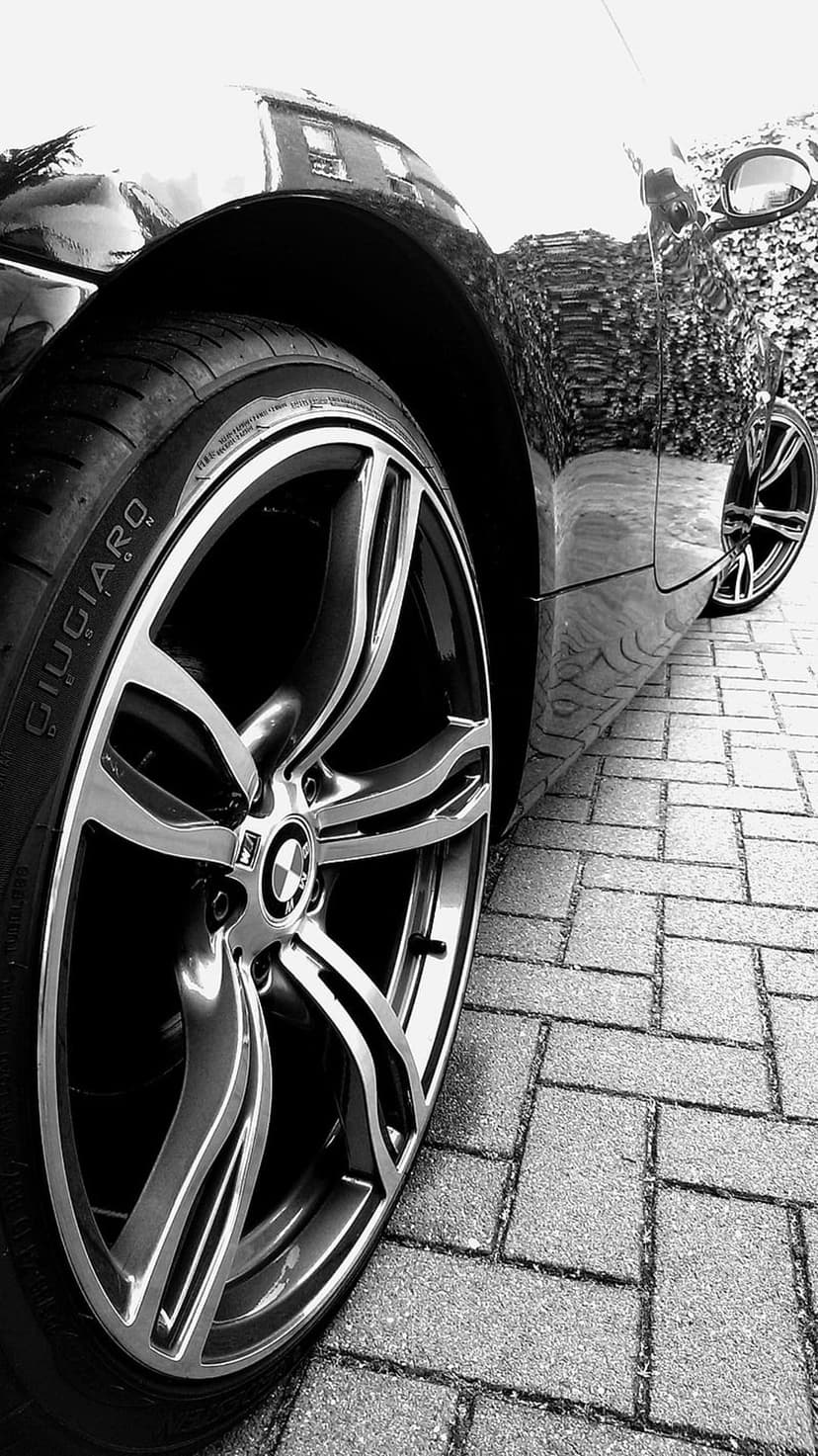 Giugiaro luxury car wheel with a polished alloy rim reflecting a brick building in black and white tones.