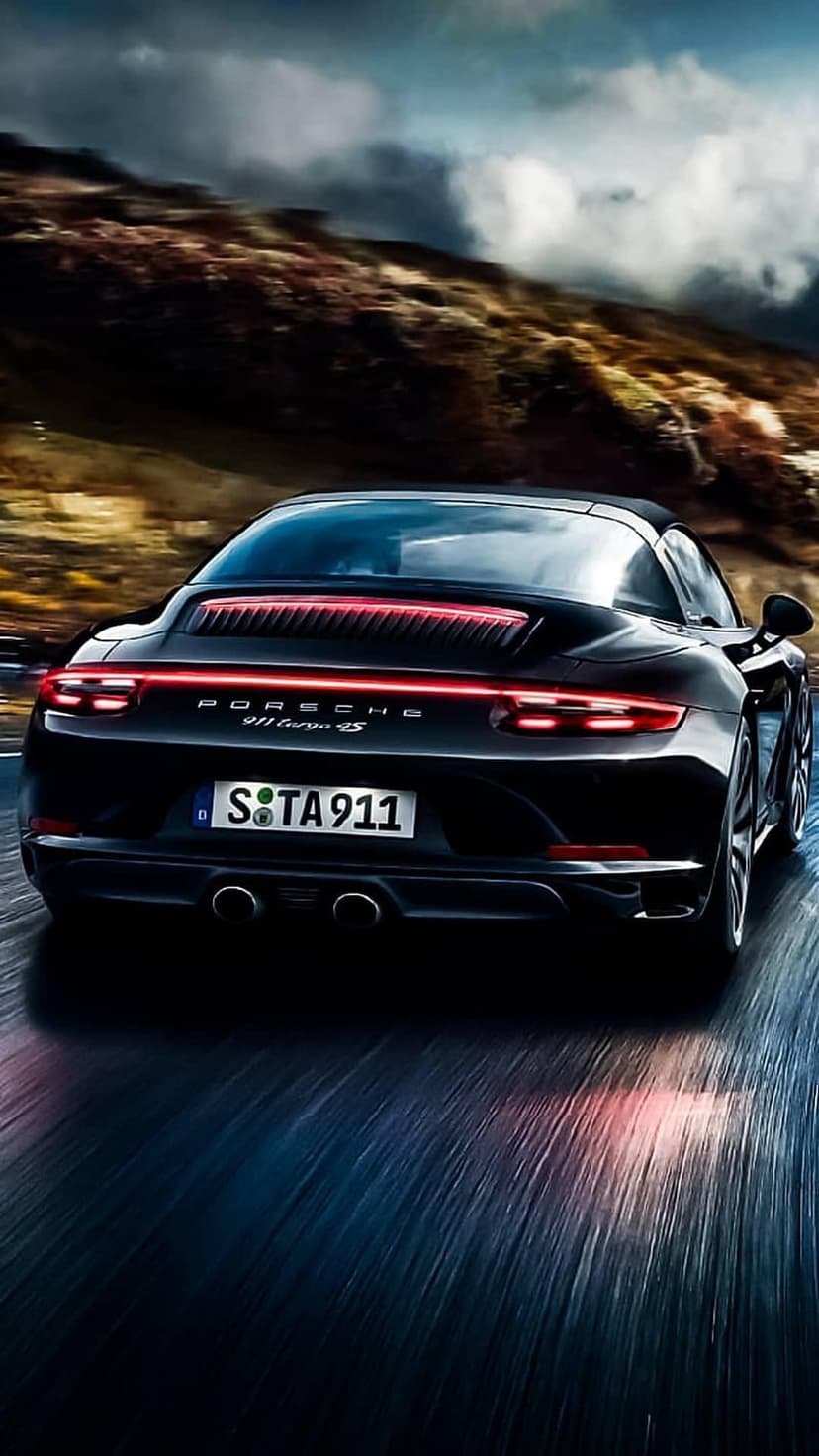 Black Porsche 911 Targa 4S speeding on a winding mountain road with motion-blurred scenery and grey clouds.