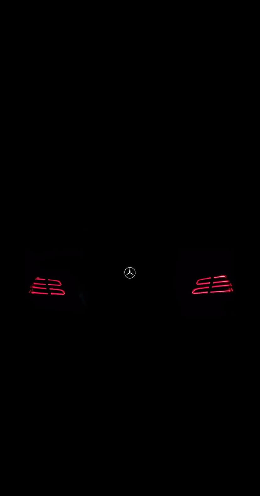 Mercedes-Benz LED taillights and chrome star emblem glow amidst deep shadows in a minimalist night scene.