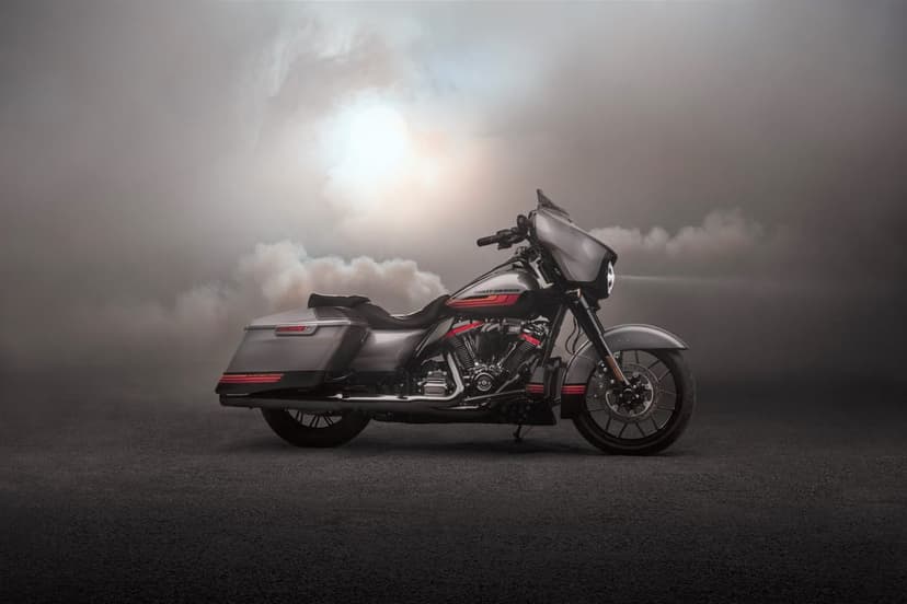 Silver Harley-Davidson motorcycle parked on dark road surrounded by thick grey smoke under a bright backlight.