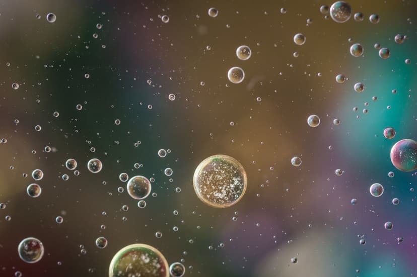Spherical oil bubbles float across a blurred iridescent background of green, blue, and purple liquid hues.