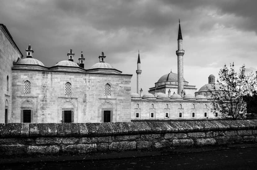Multiple mosque domes and minarets stand behind a stone wall under a dark, cloudy sky in a grayscale photograph.
