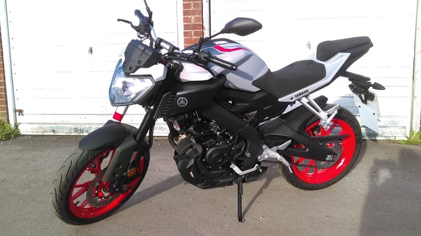 Yamaha MT-125 motorcycle with red wheels and silver bodywork parked on asphalt against white garage doors.