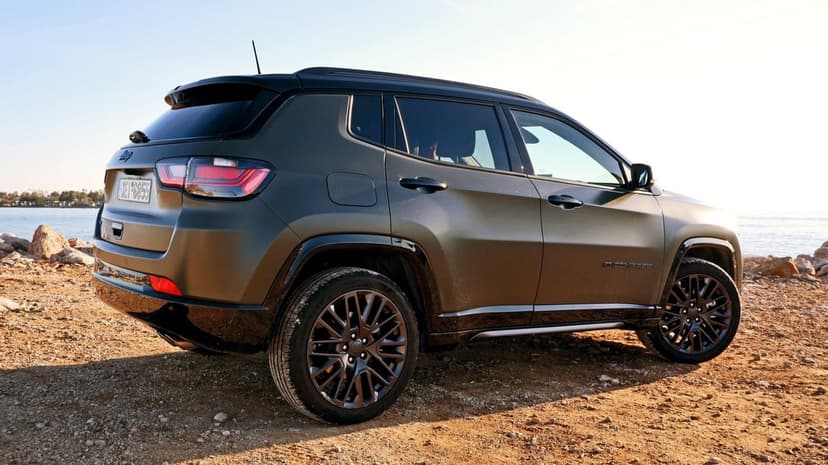 Matte green Jeep Compass SUV parked on a rocky beach at sunset with dark alloy wheels and sea background.