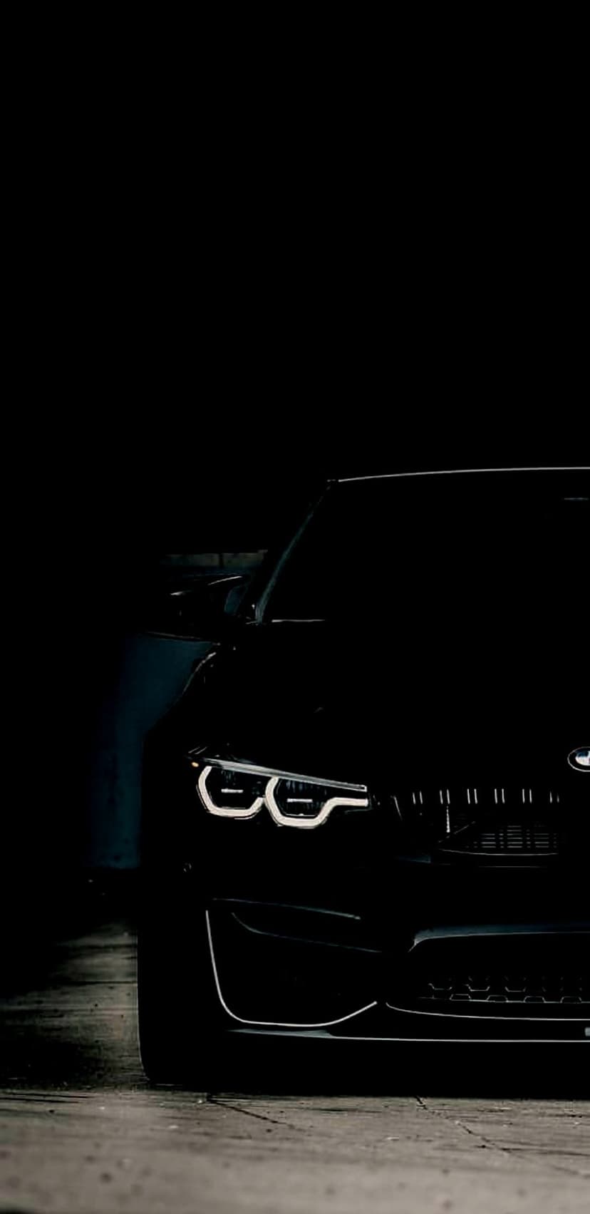 BMW M4 LED headlights and grille glow in a dark concrete garage with dramatic low-angle shadows and reflections.