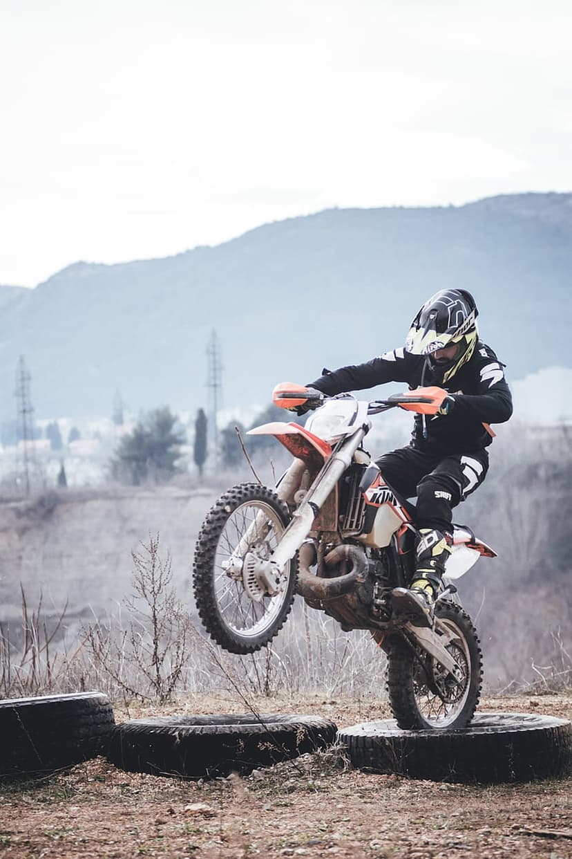 Motocross rider jumping a dirt bike over large tires with a hazy mountain landscape and power lines in the distance.