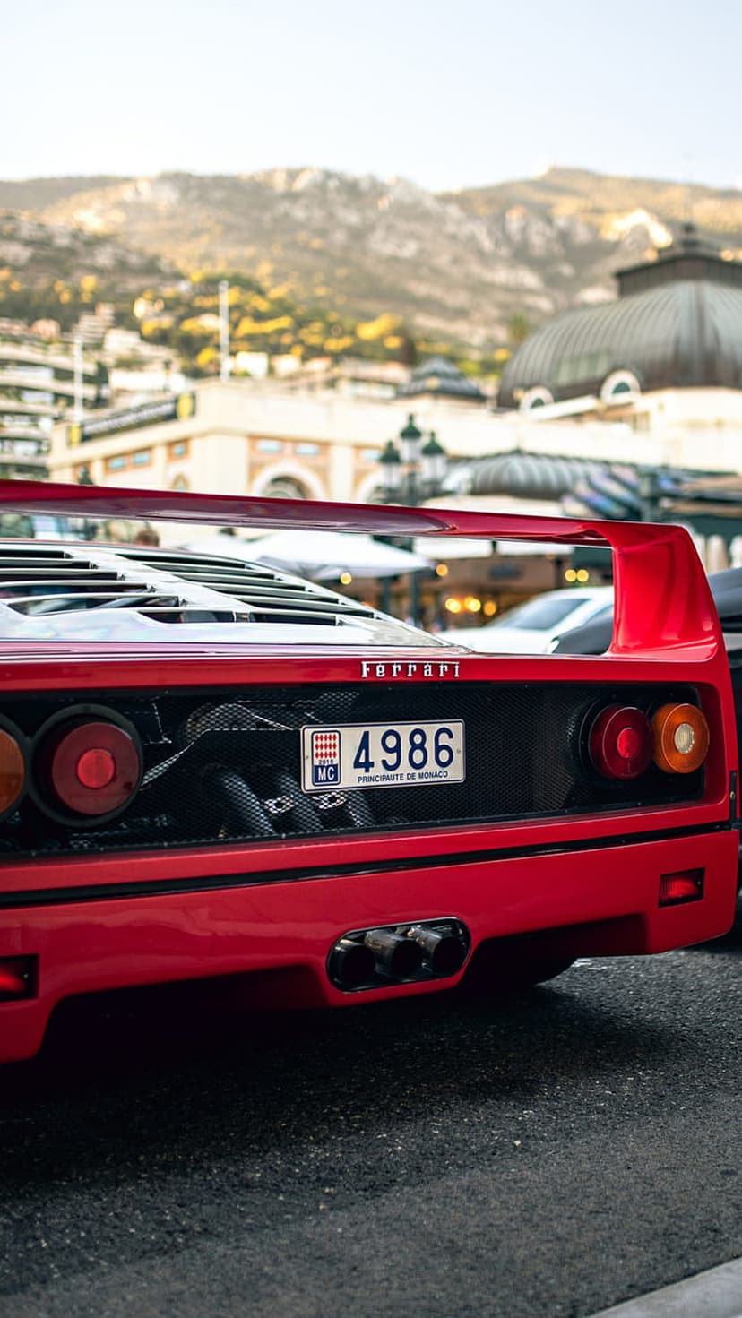 Ferrari F40 rear view with a red spoiler, quad exhaust pipes, and a Monaco license plate on a European street.