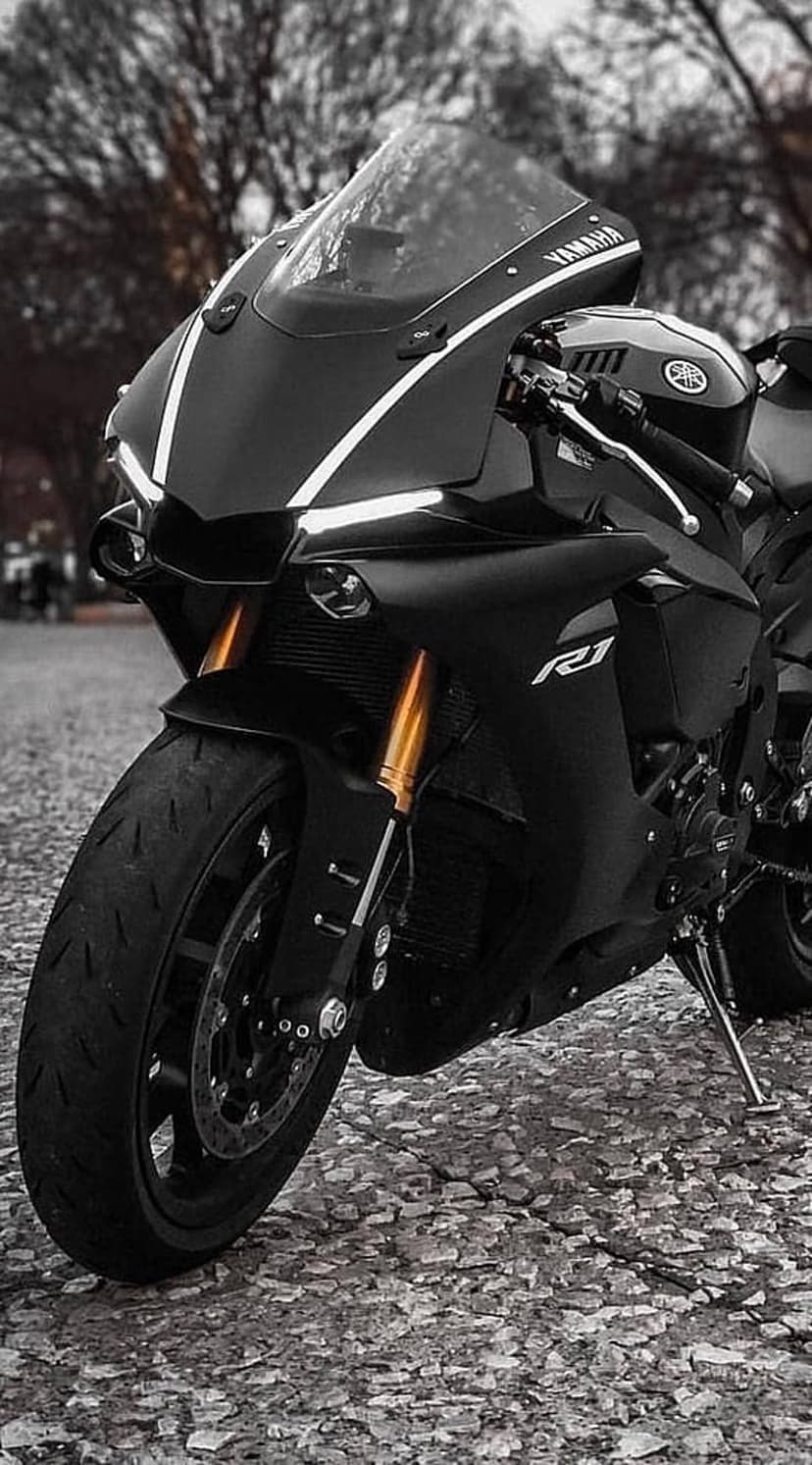 Yamaha R1 motorcycle in matte black with LED headlights and front suspension against a blurred nature background.