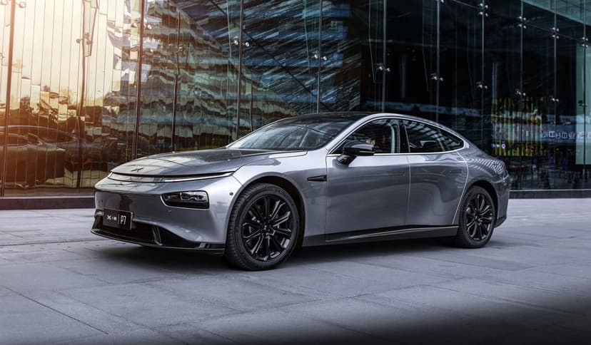Silver electric sedan parked on a stone walkway in front of a reflective glass skyscraper at sunset.