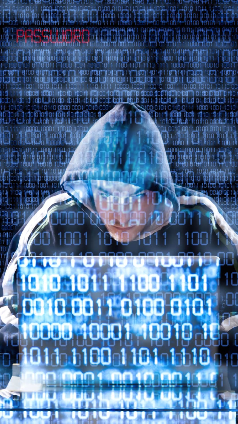 Hooded figure with a blue binary code face mask typing on a laptop amidst red and blue digital data streams.