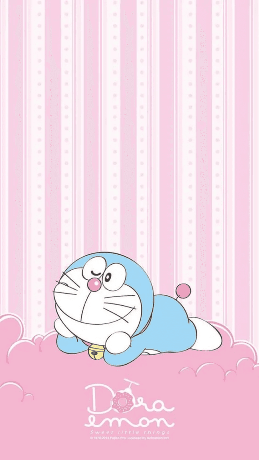 Doraemon sleeps on a soft pink cloud over a vertically striped pink background with a small golden bell visible.