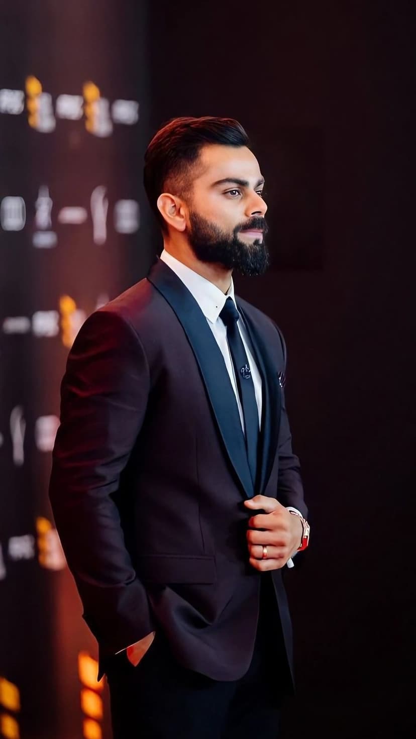 Virat Kohli adjusts his maroon tuxedo jacket with navy lapels while sporting a sharp beard and neat hairstyle.