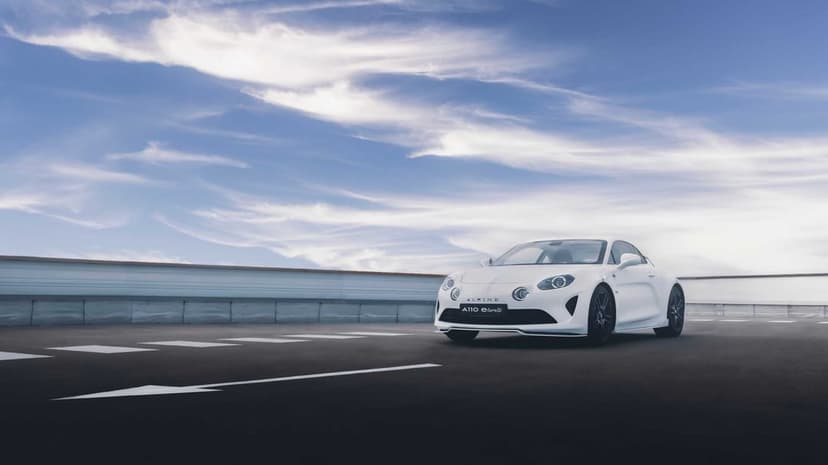 White Alpine A110 E-ternité electric sports car on asphalt under a vast blue sky with wispy white clouds.