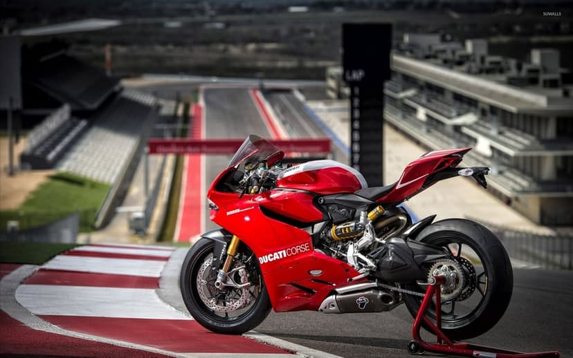 Red Ducati 1199 Panigale superbike on a professional race track with grandstands and a tower in the background.