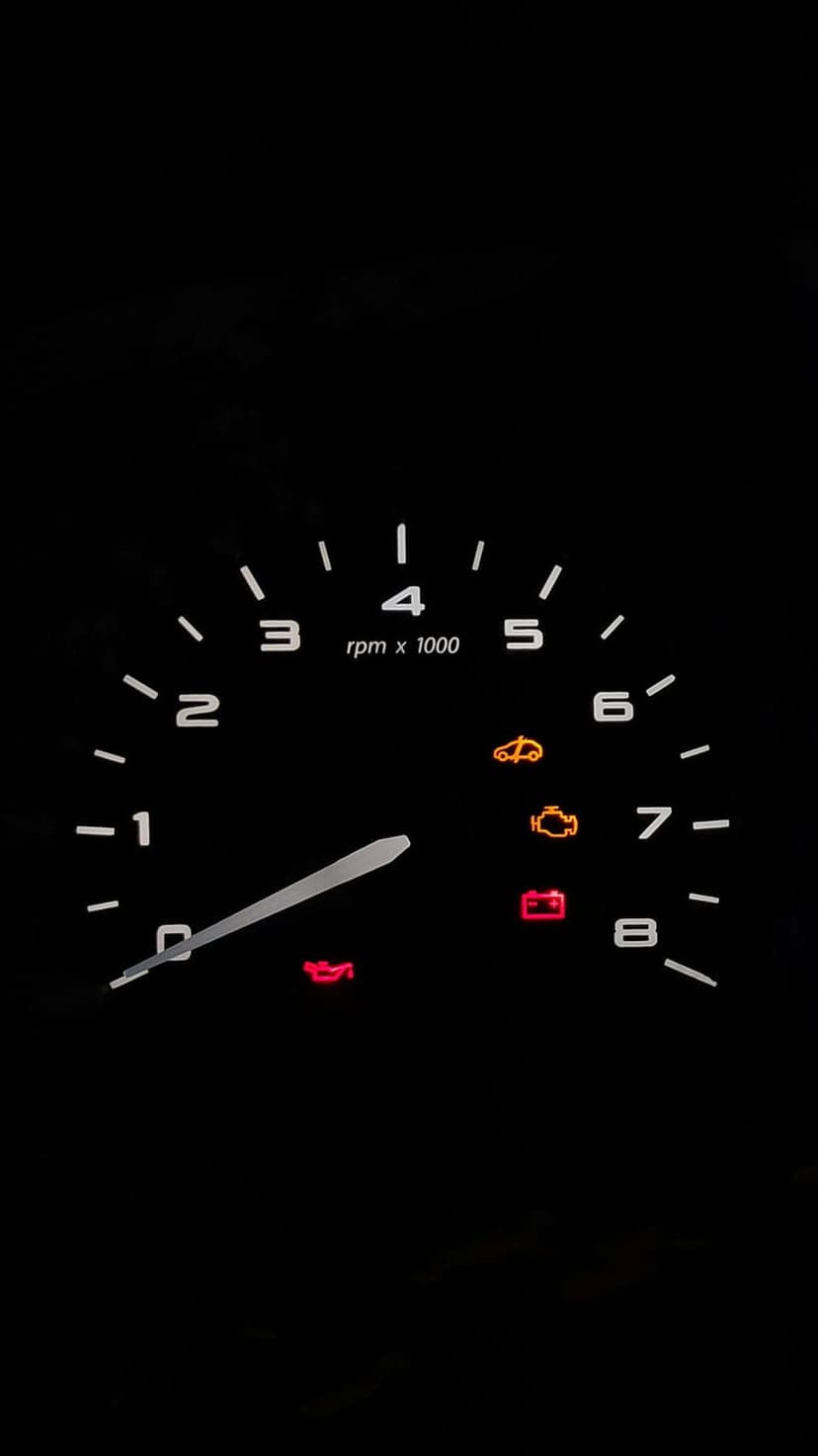 Car tachometer and glowing dashboard warning lights illuminated in amber and red during a nighttime drive.