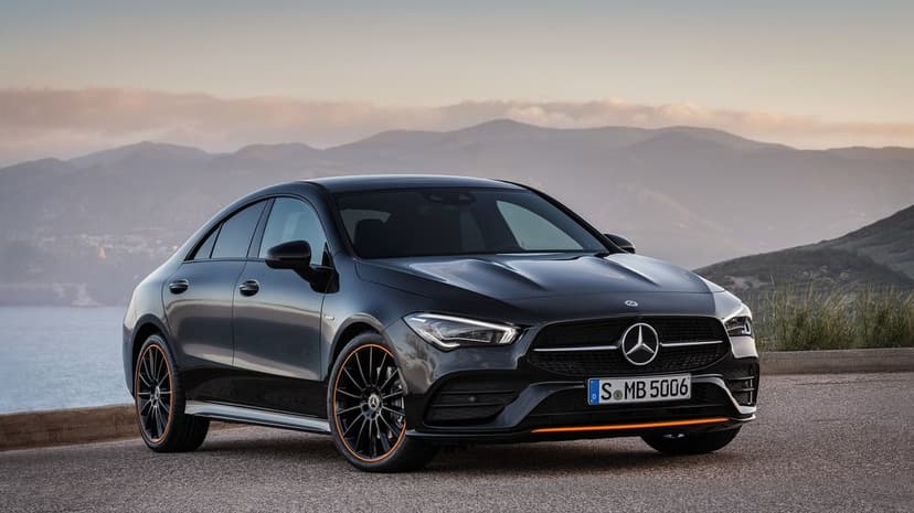 Black Mercedes-Benz CLA with orange accents parked on a scenic coastal road with mountains in the background.
