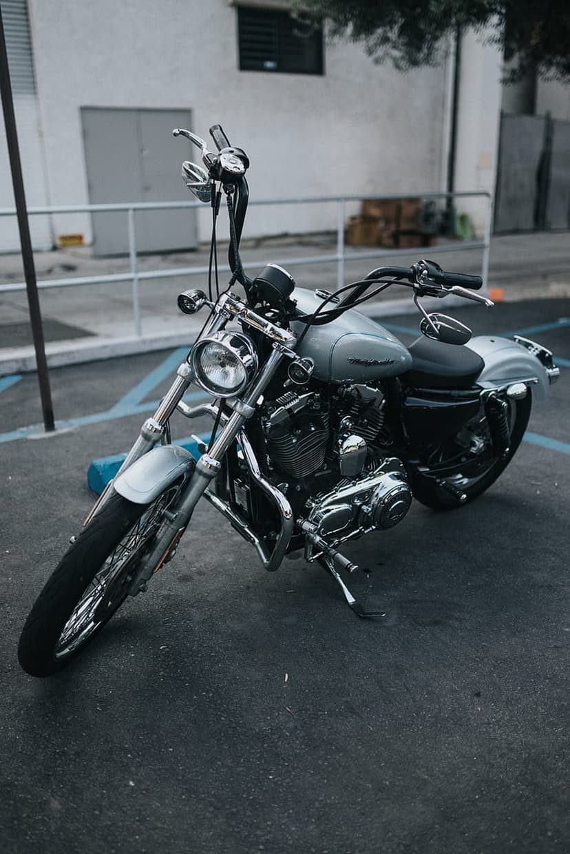 Silver Harley Davidson motorcycle with chrome accents parked on asphalt against a soft industrial backdrop.