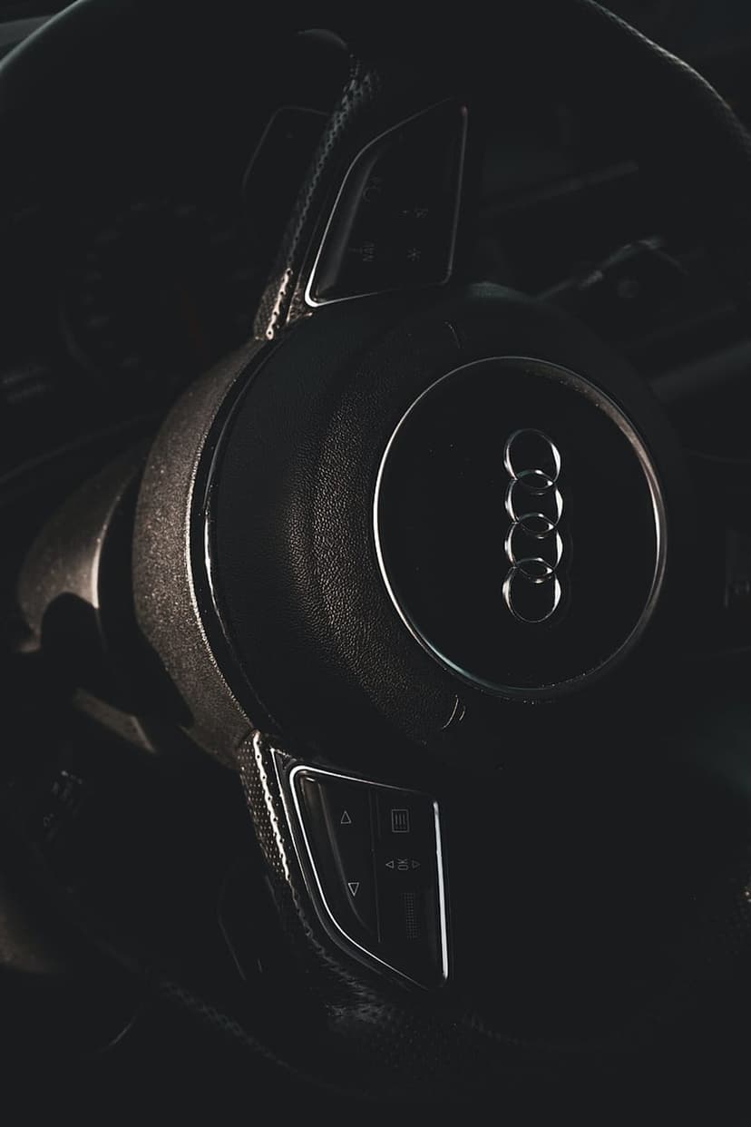 Audi steering wheel with chrome rings and integrated buttons visible through dramatic low-light shadows.