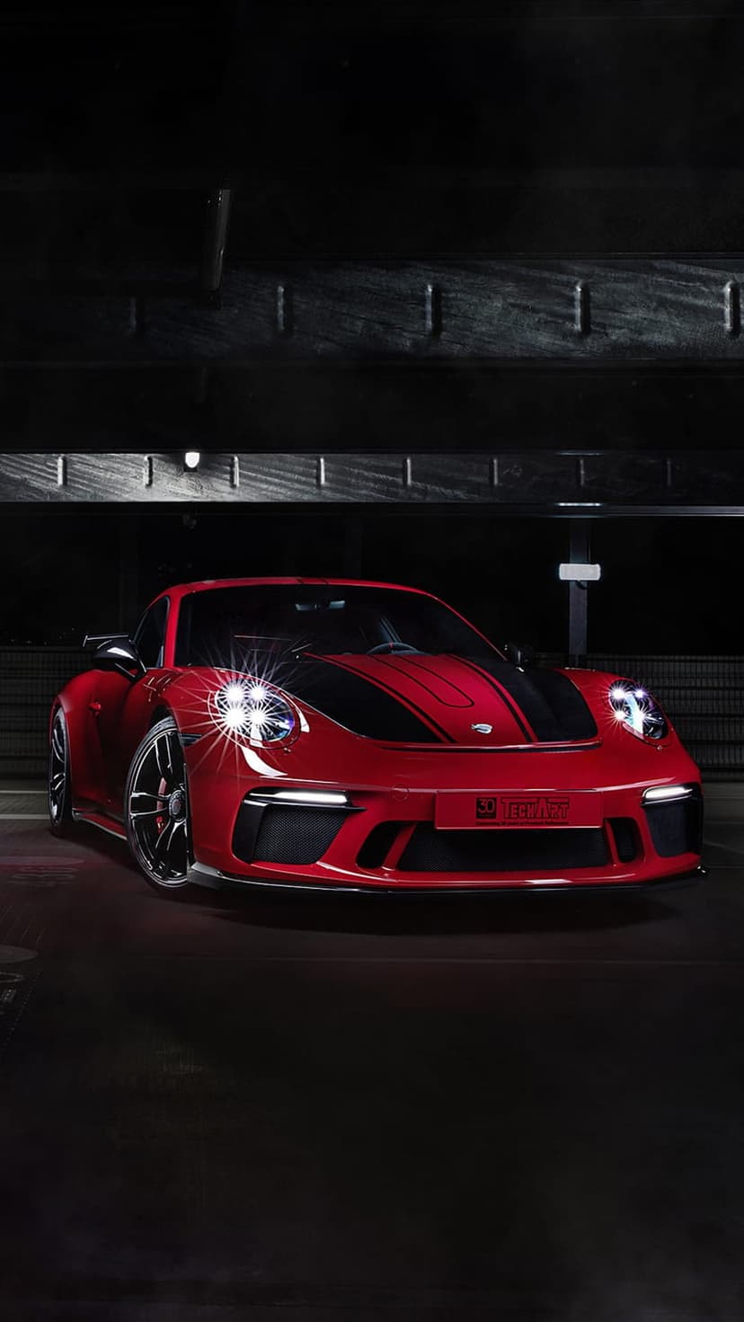 Red Porsche 911 GT3 RS featuring black racing stripes and lit LED headlights parked in a dark studio.