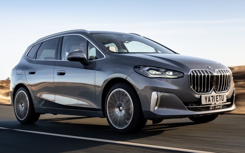 Modern grey BMW driving on a paved road under a clear sky with motion blurred wheels and silver trim.