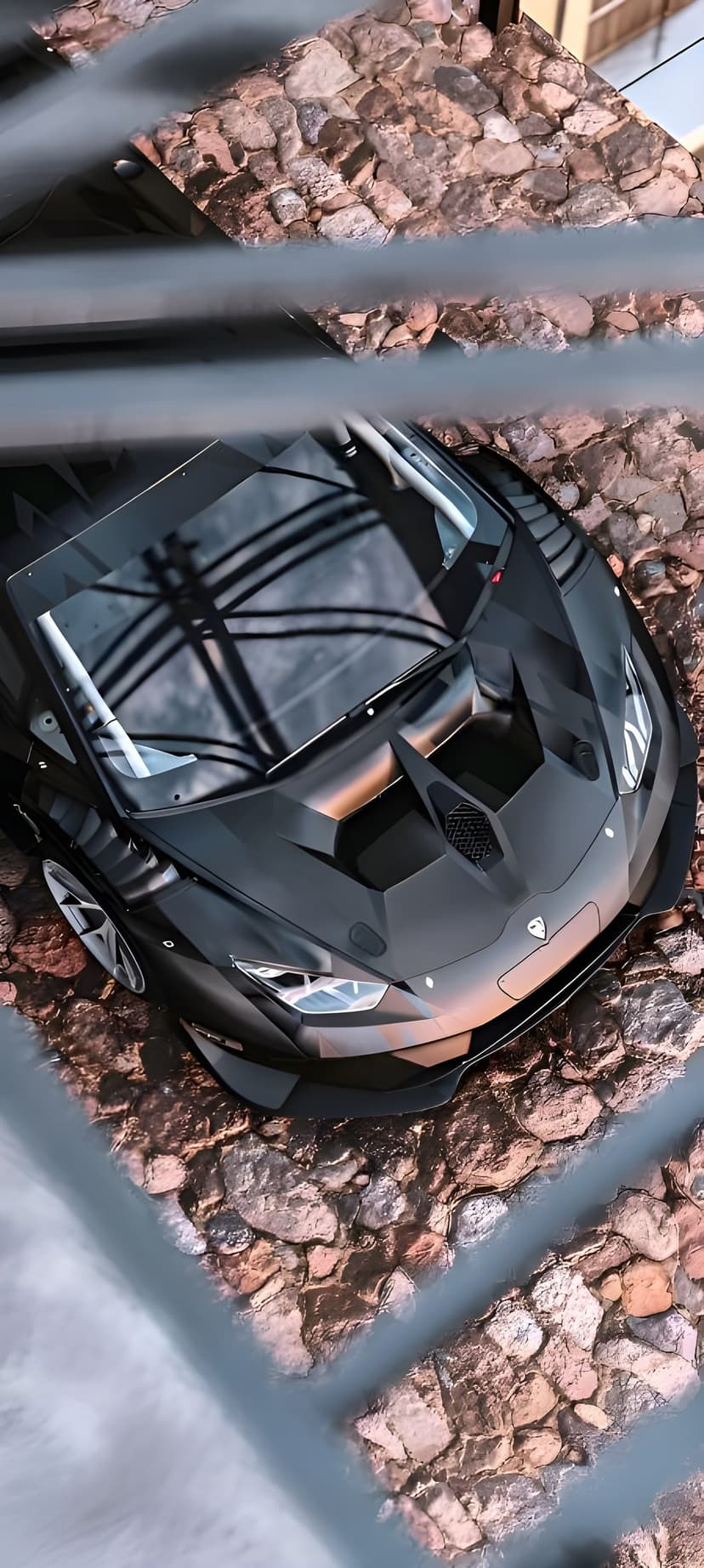 Matte black Lamborghini Aventador parked on earthy stones, showing sharp aerodynamic lines from a high angle.