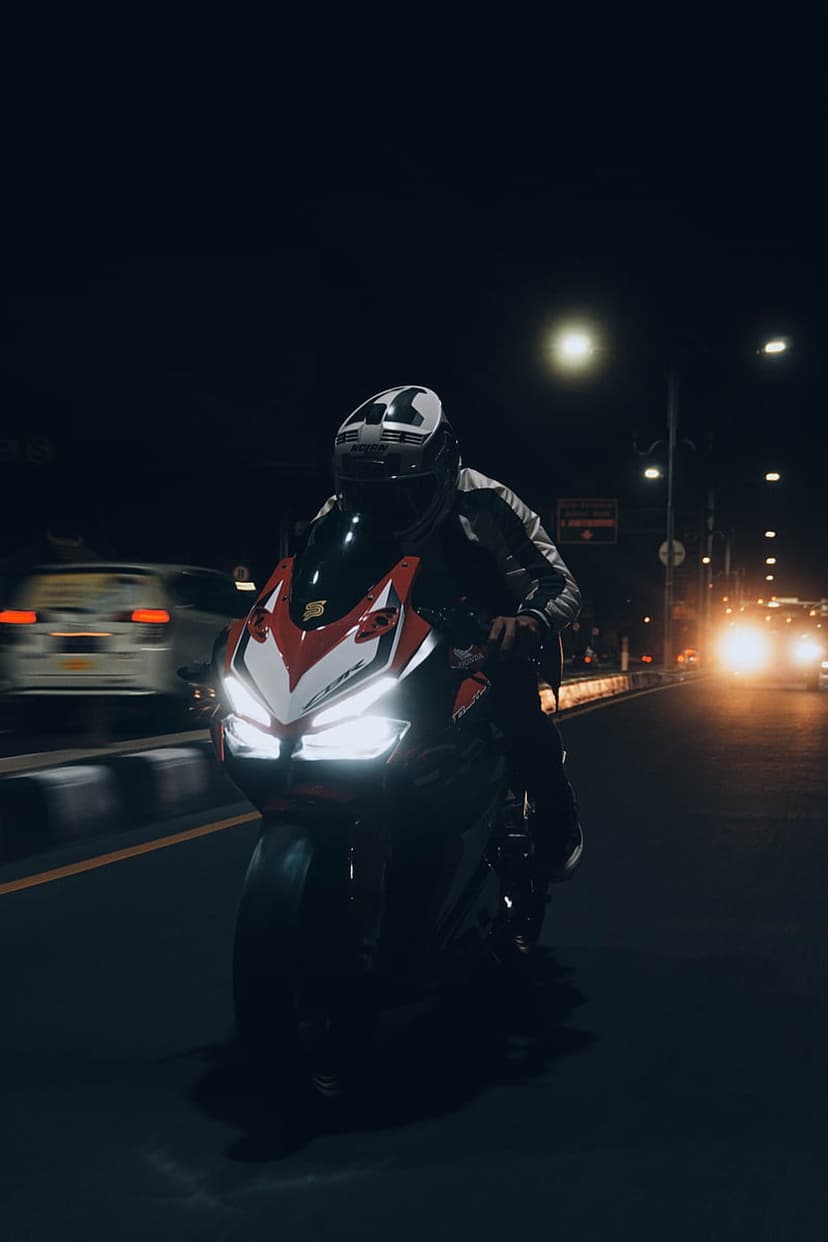 Motorcyclist in a helmet on a red and white sportbike riding through a dark city street with glowing headlights.