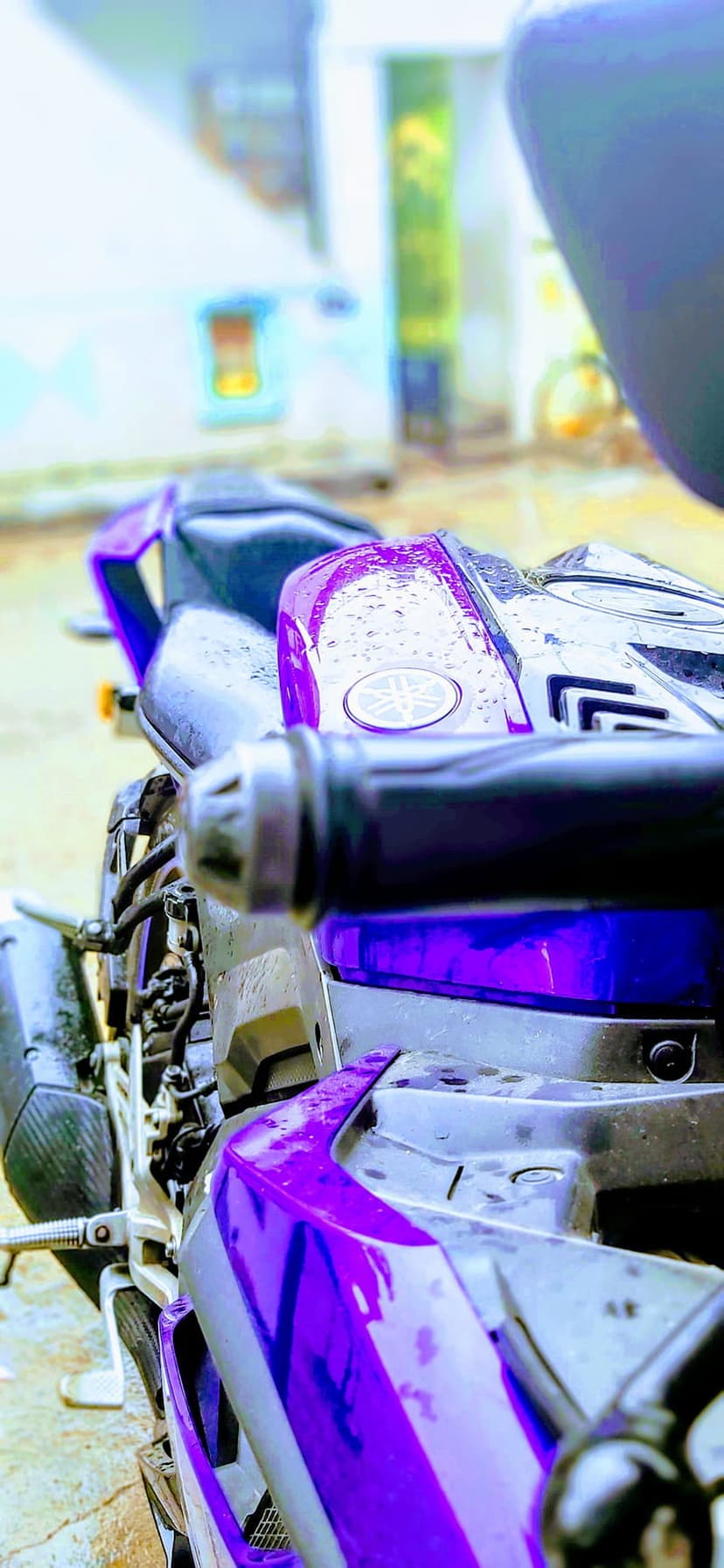 Purple Yamaha motorcycle features tiny water droplets on its metallic fairing and seat in a post-rain closeup.