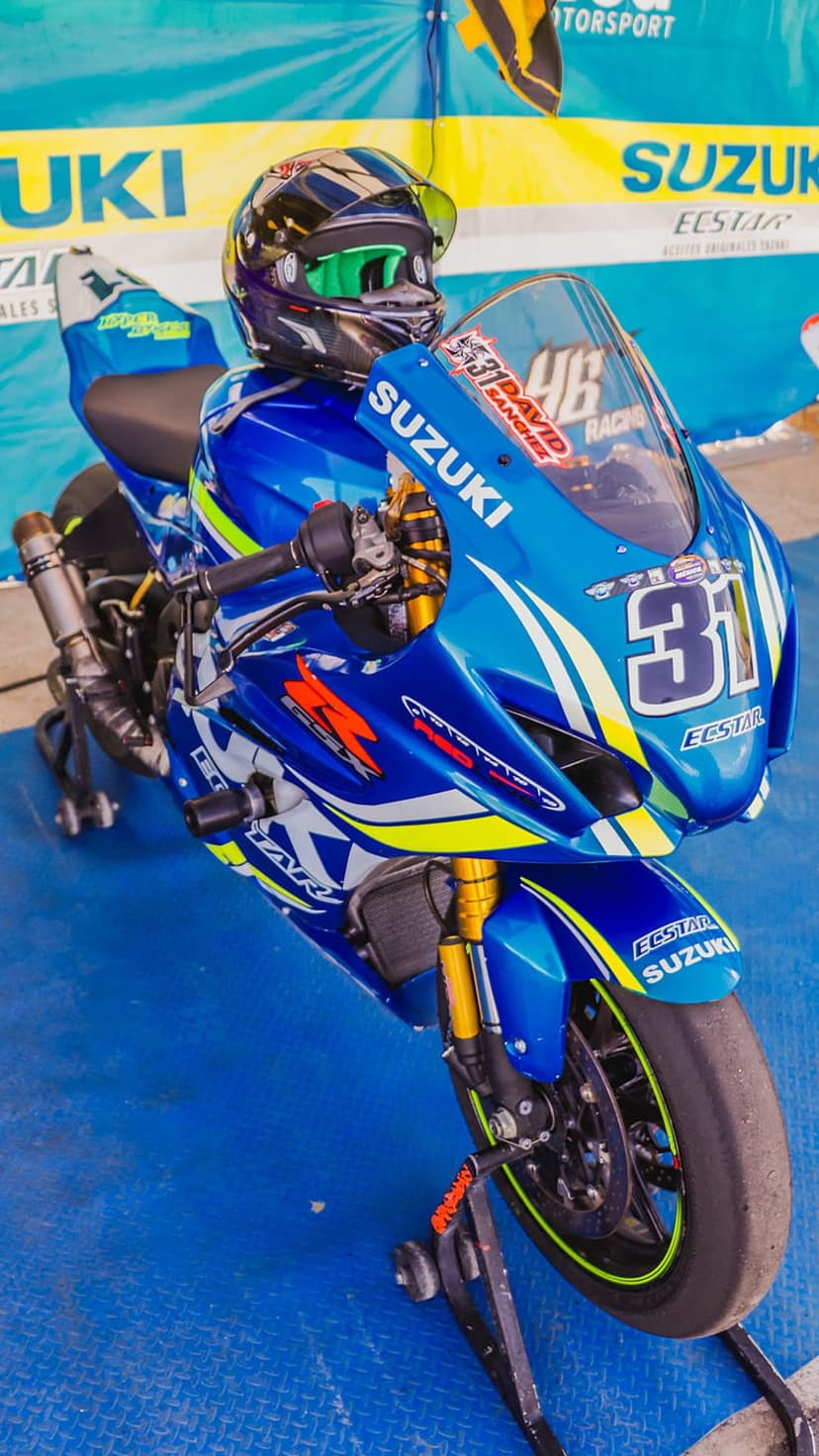 Suzuki racing motorcycle with blue ECSTAR decals positioned next to a black and neon green helmet.