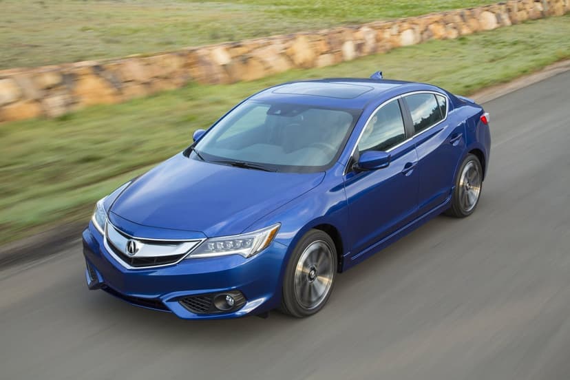 Blue Acura ILX luxury sedan driving fast on a paved road past a stone wall and green fields with motion blur.