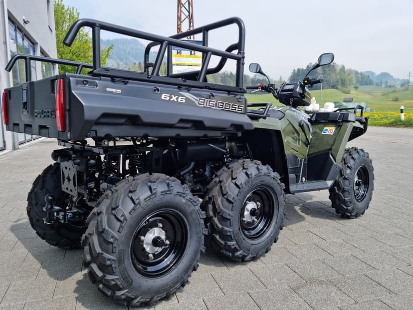 Polaris 6x6 Big Boss ATV with olive green body and six heavy-duty tires parked on a stone paved driveway.