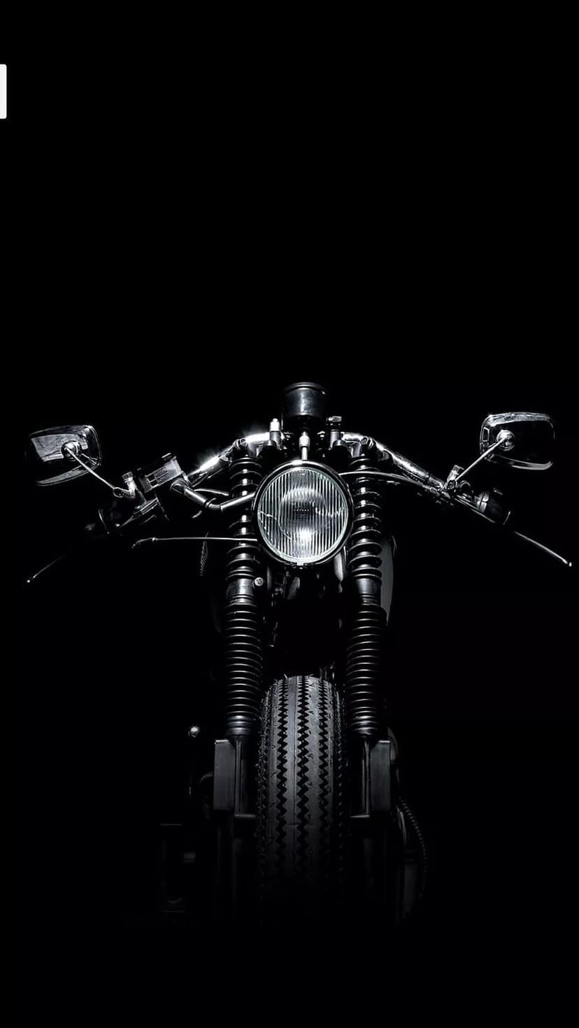 Vintage motorcycle headlight and textured tire shown in high-contrast black and white against a dark background.