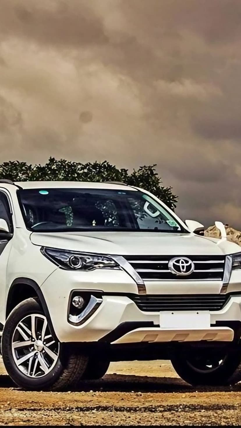 White Toyota Fortuner SUV parked outdoors featuring a chrome grille and headlights under a cloudy, overcast sky.
