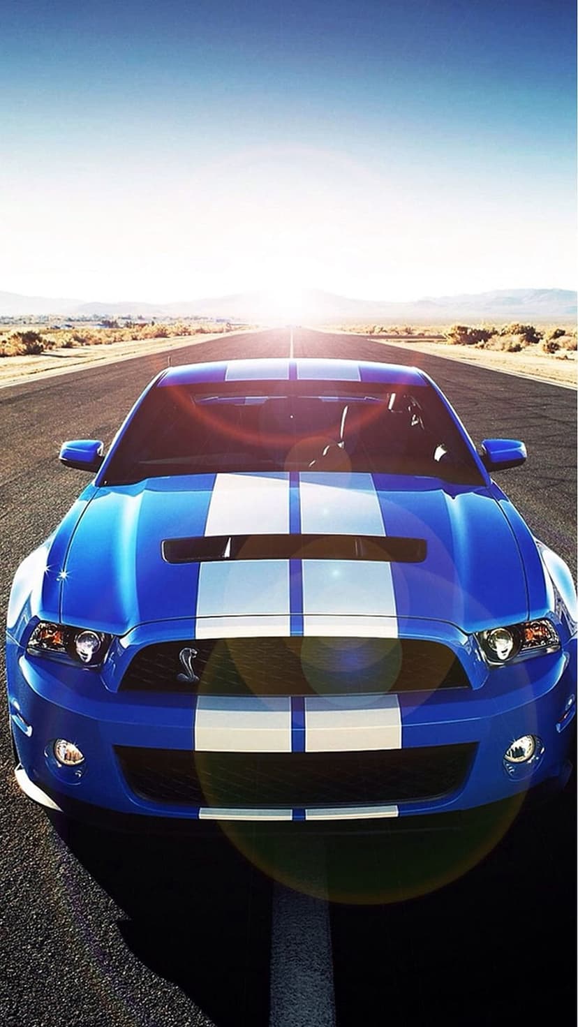 Blue Ford Mustang GT500 with white stripes on a sunny desert road, captured from a low front-facing perspective.