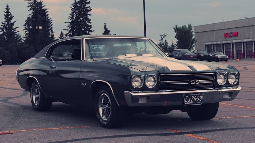 Dark green 1970 Chevrolet Chevelle SS with white racing stripes parked in a lot during a moody cloudy sunset.